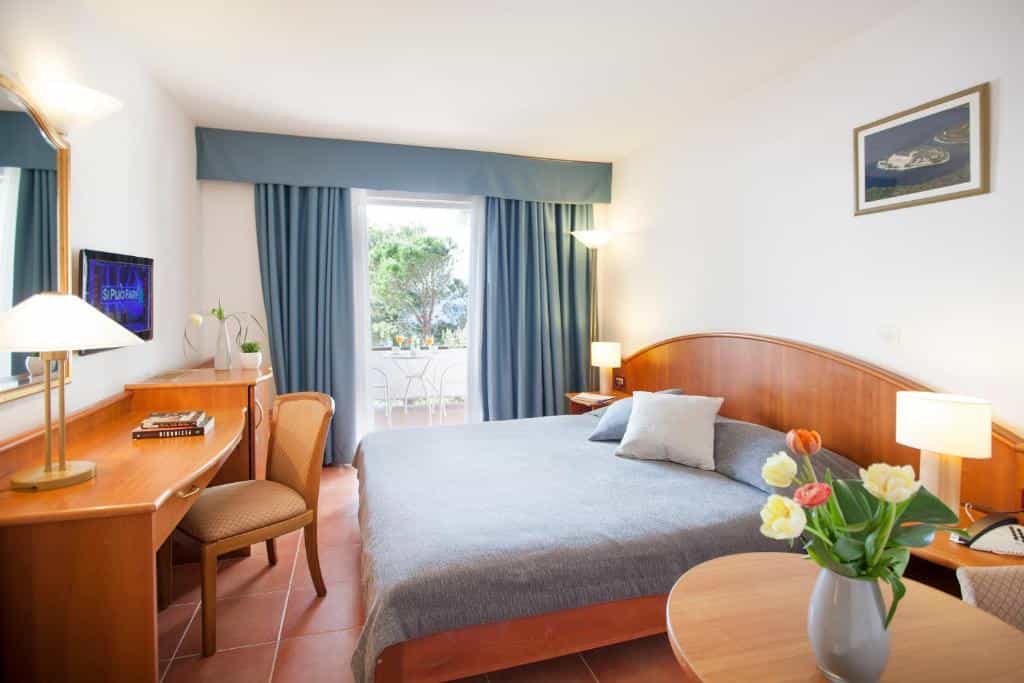 Hotel room with wooden furniture, blue curtains, and balcony view of trees, Odisej Mljet.