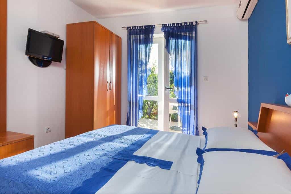 Bedroom with blue bedding, wooden wardrobe, and balcony door with sheer blue curtains