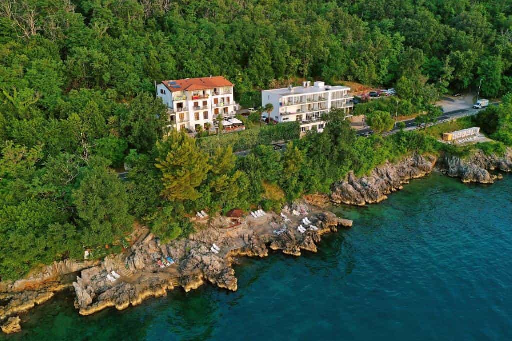 Hotels nestled in dense green forest above rocky coastline and clear blue water