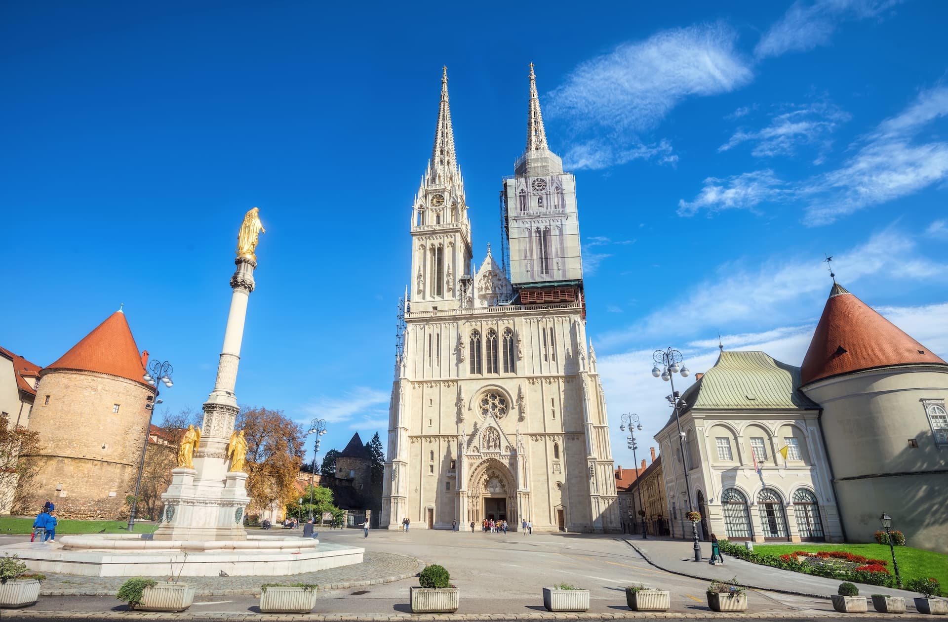 Cathedral and Blessed Virgin Mary monument in Zagreb square under blue sky.