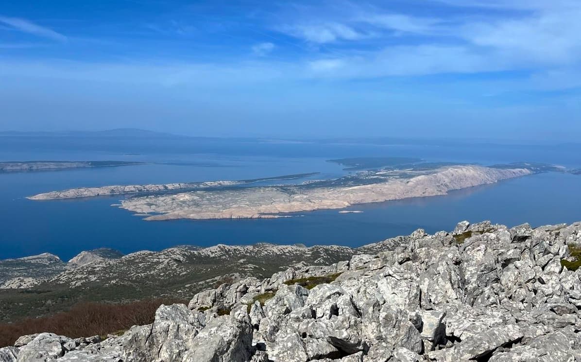 Rocky mountain summit overlooking arid islands in deep blue sea under clear sky