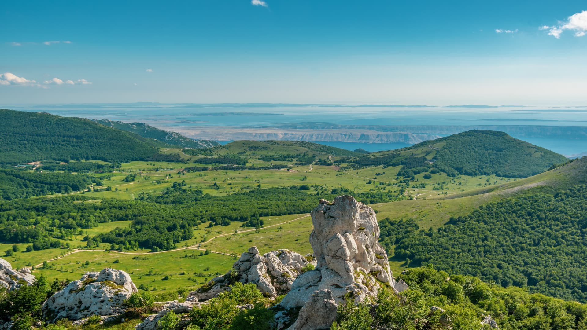 Panorama of Baske Ostarije village with green hills, rocky outcrops, and distant sea view.