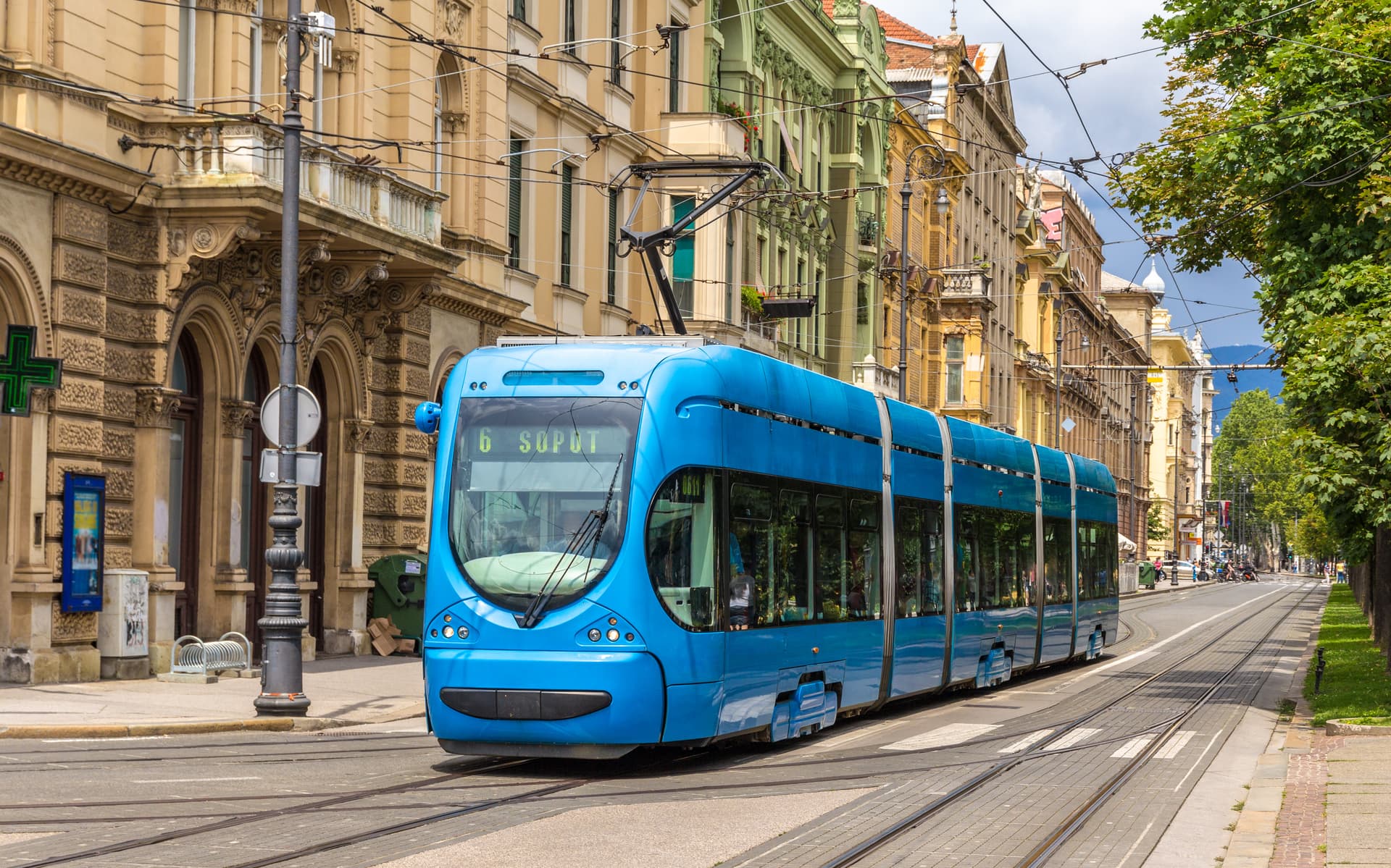 Blue modern tram operating on tracks past historic buildings in Zagreb.