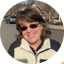 Woman smiling outdoors wearing sunglasses and a fleece jacket on a residential street.