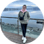 Person standing on a wooden deck overlooking a calm lake with snow-covered mountains in the background.