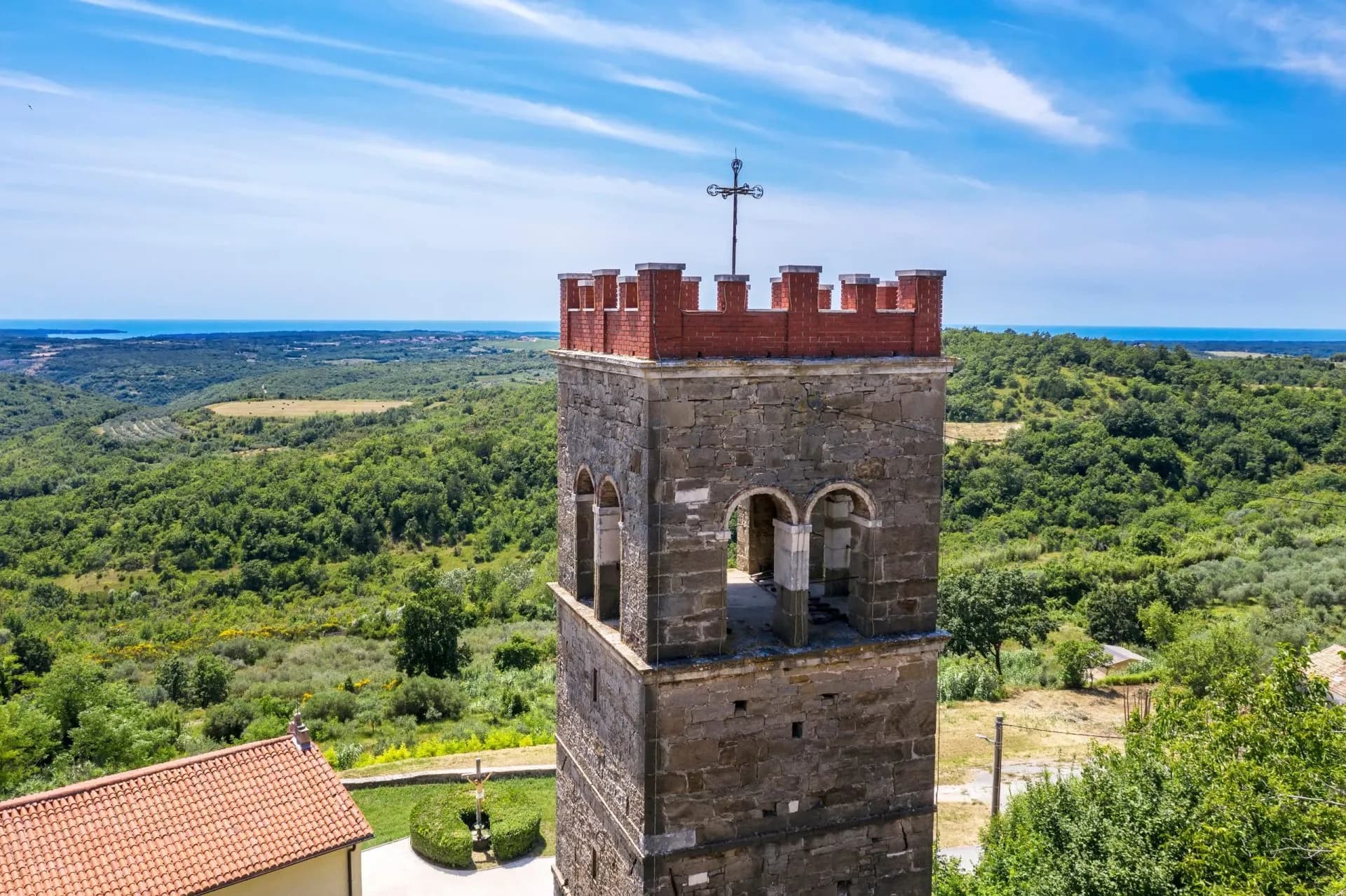 Stone bell tower with crenellations overlooking lush green hills toward the sea in Krasica, Istria.