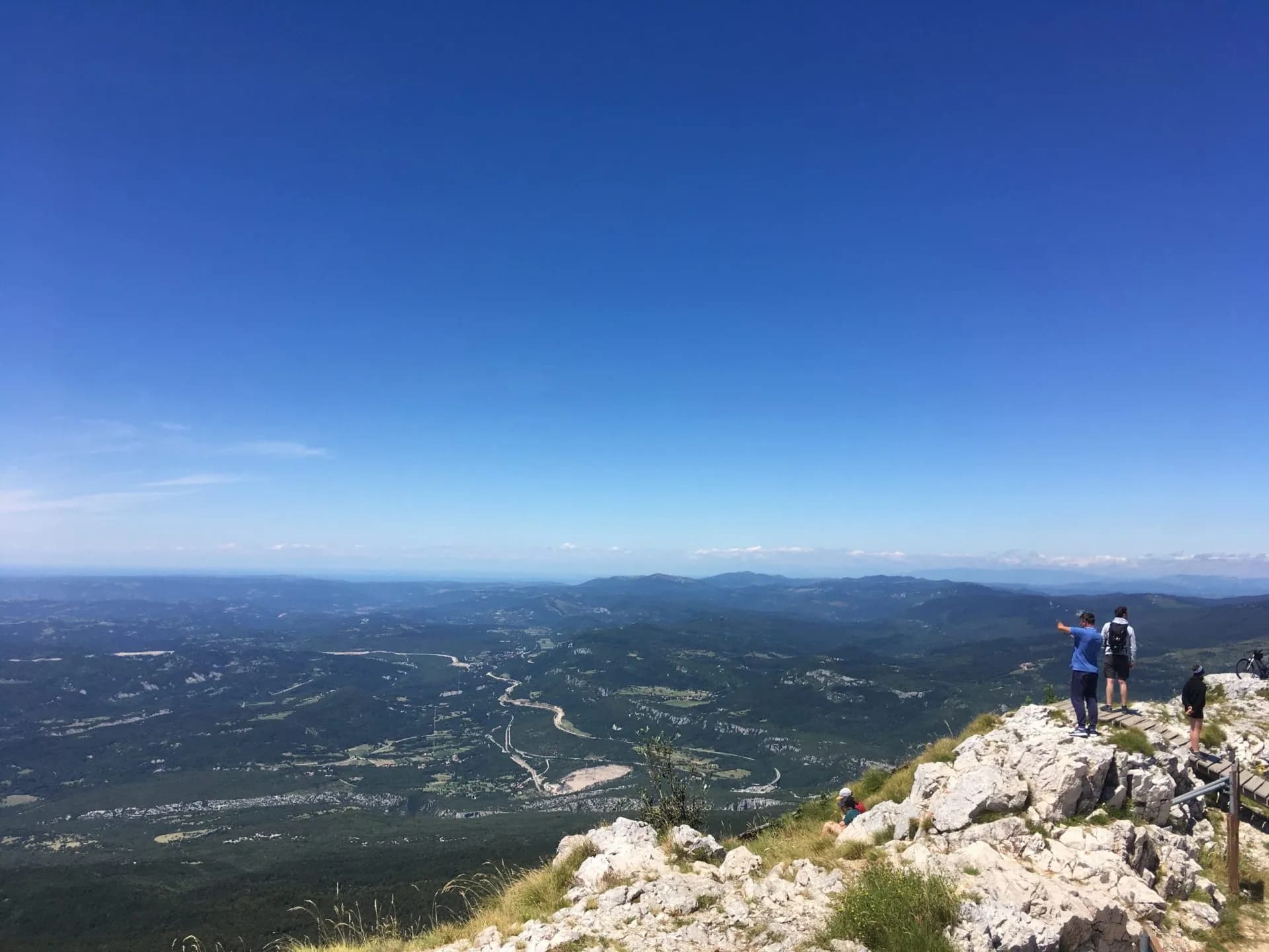 Hikers enjoying panoramic view from rocky summit overlooking green valleys under clear blue sky at Učka Gora.