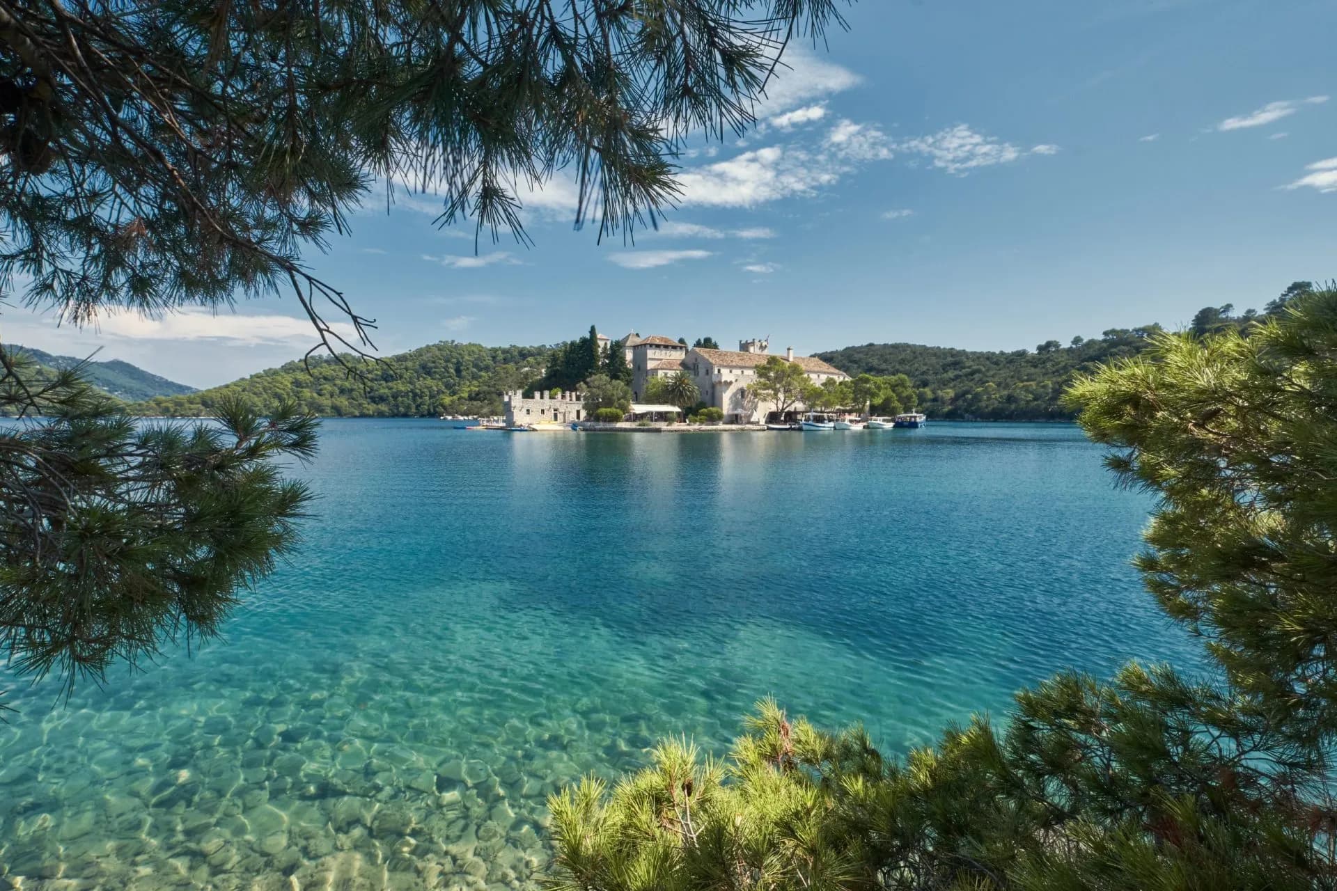 Saltwater lake with clear turquoise water, historic buildings on an island, framed by pine branches.