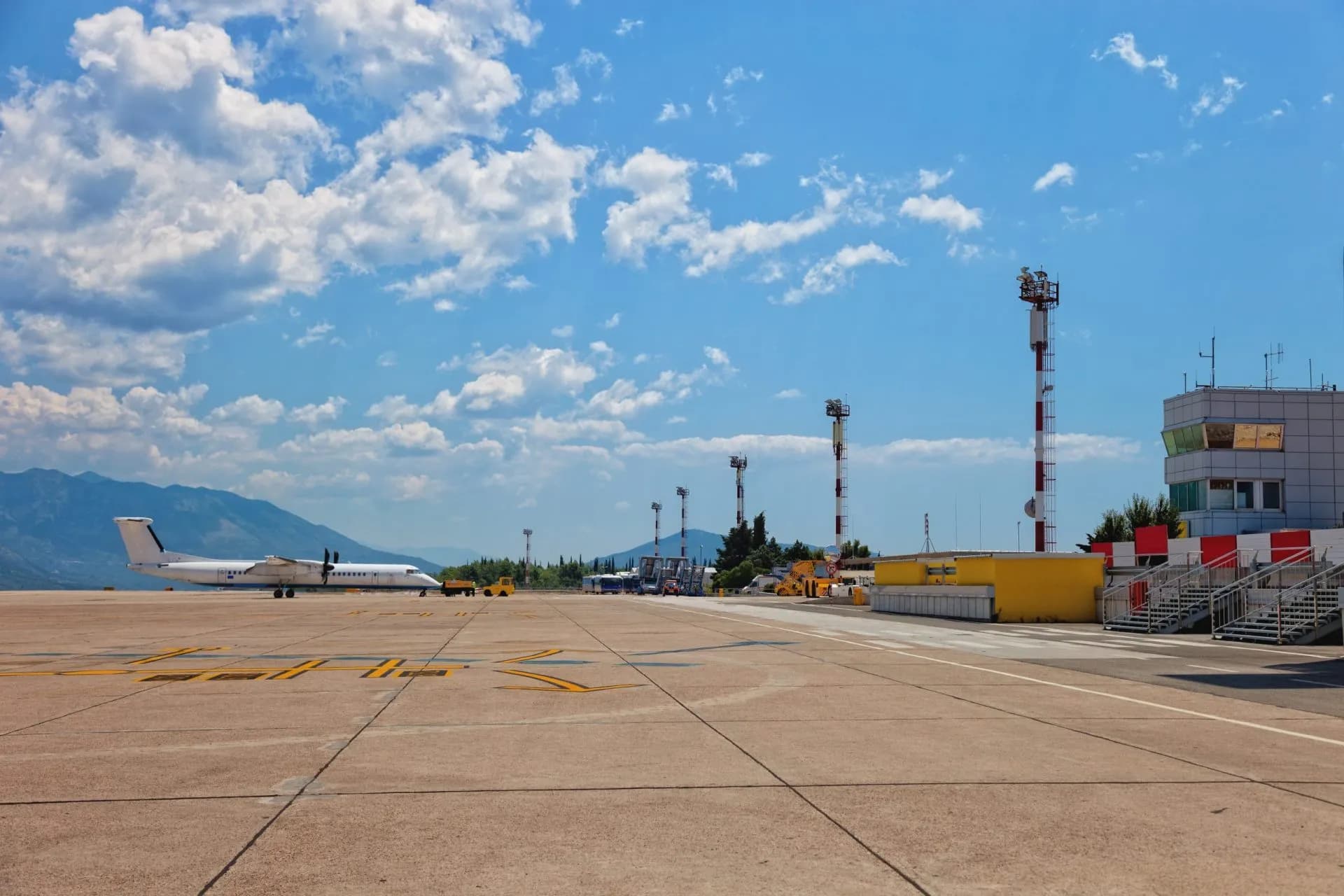 Turboprop airplane on tarmac at Dubrovnik Airport with mountains and blue sky.