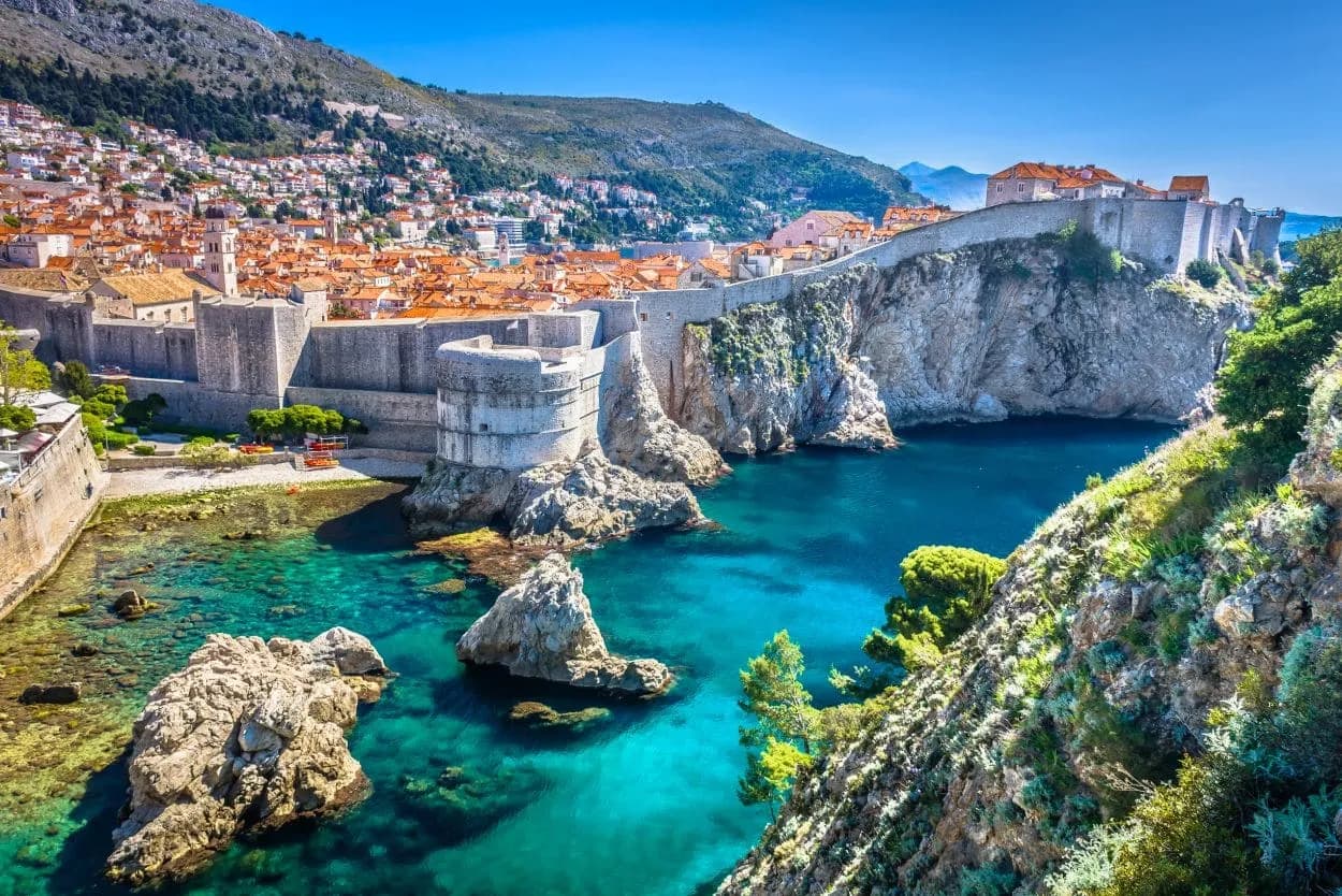 Dubrovnik city walls overlooking turquoise Adriatic Sea cove with steep, rocky coastline.