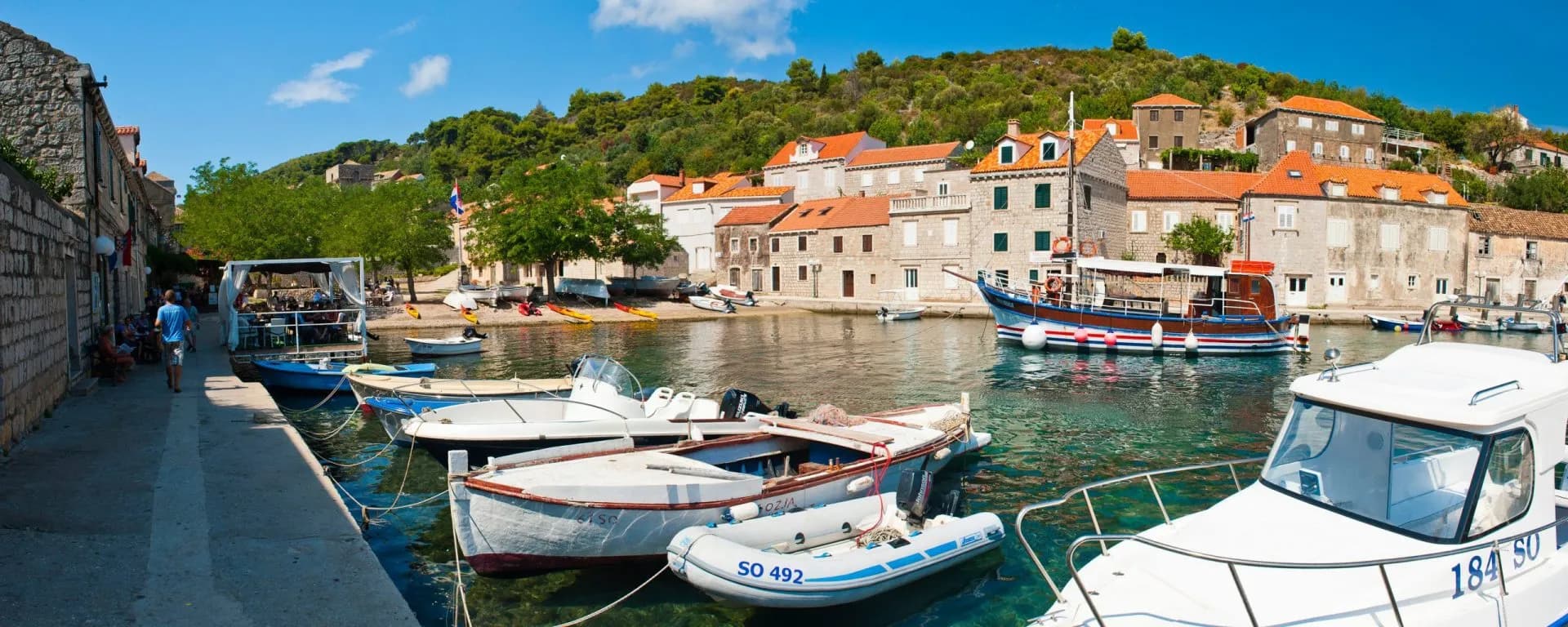 Boats docked in clear water near stone buildings with red roofs on Sipan Island.