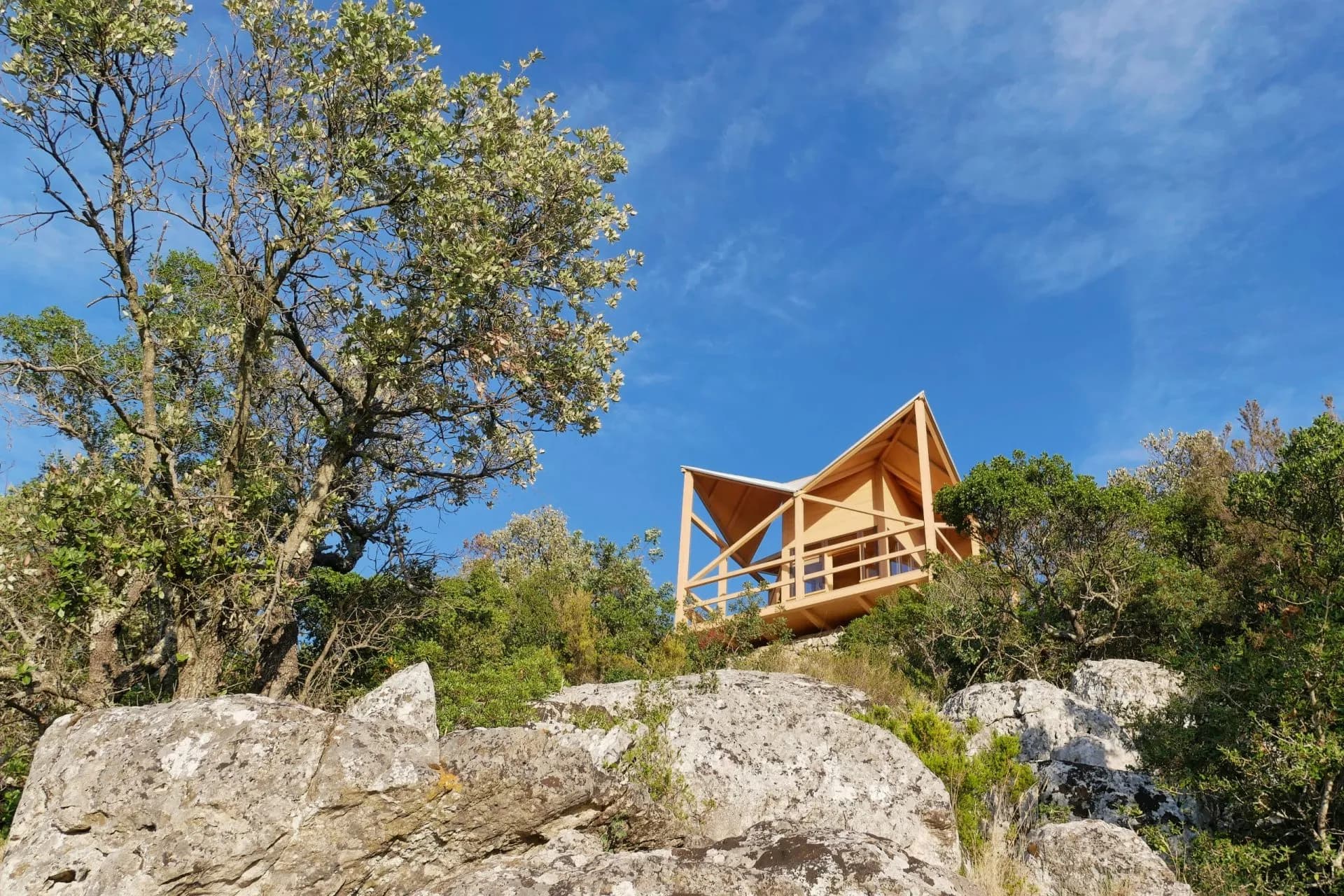 Wooden observation tower on rocky hillside with trees under bright blue sky, Montokuc