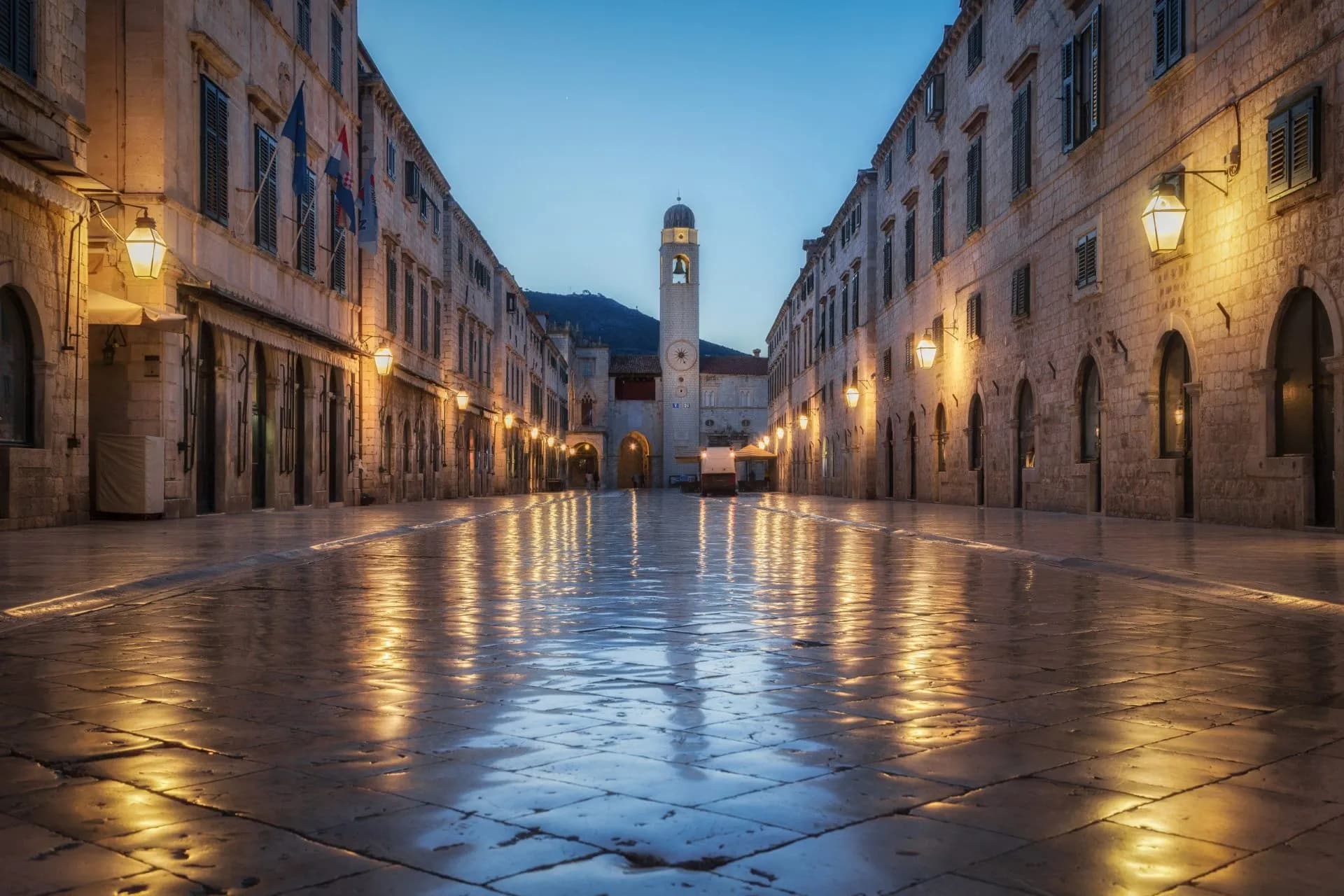 Old Town of Dubrovnik Stradun street illuminated at dusk with reflections on wet pavement toward the clock tower.