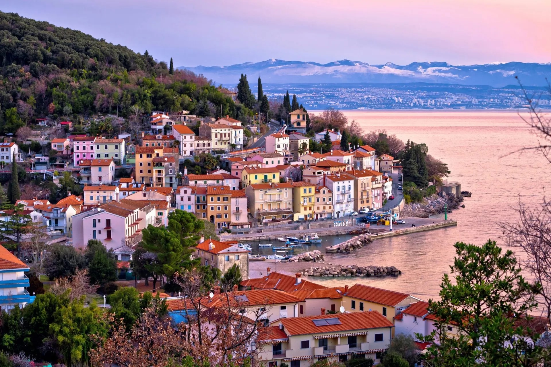 Coastal town with colorful houses on a hillside overlooking the sea and snow-capped mountains.