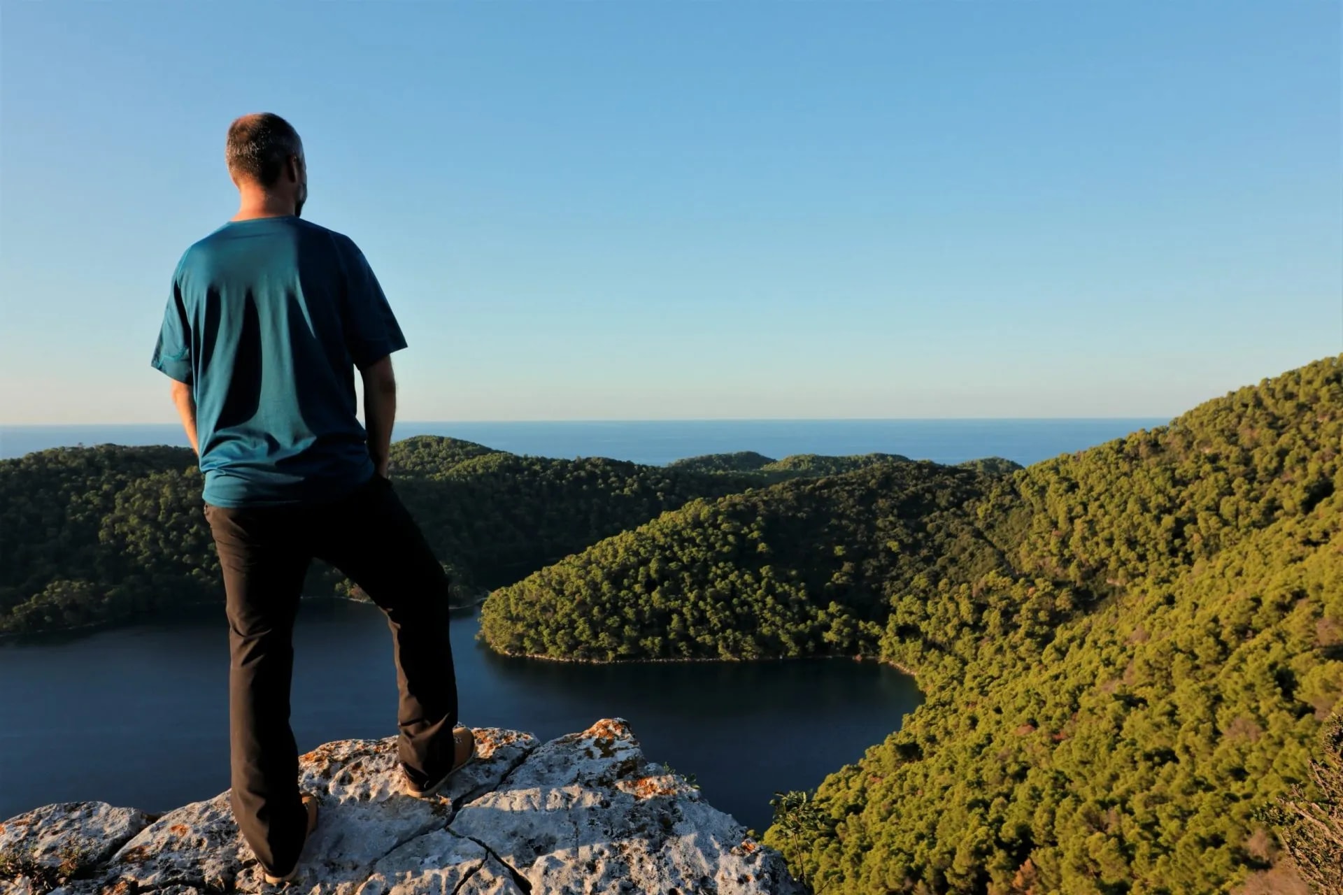 Hiker above Mljet saltwater lake looking over forested hills toward the sea.