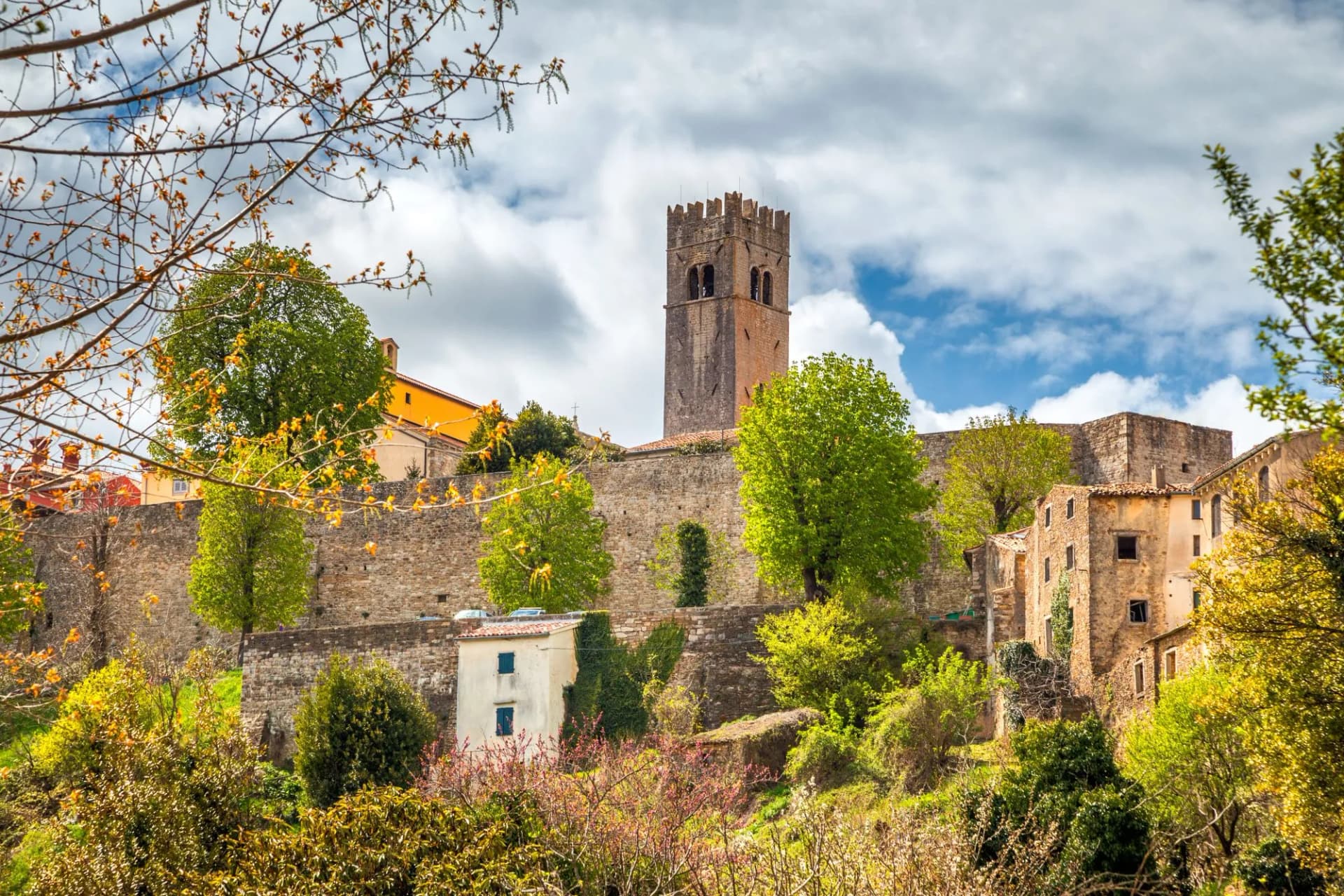 Historic stone tower above walls and old buildings in Motovun, seen through spring foliage.