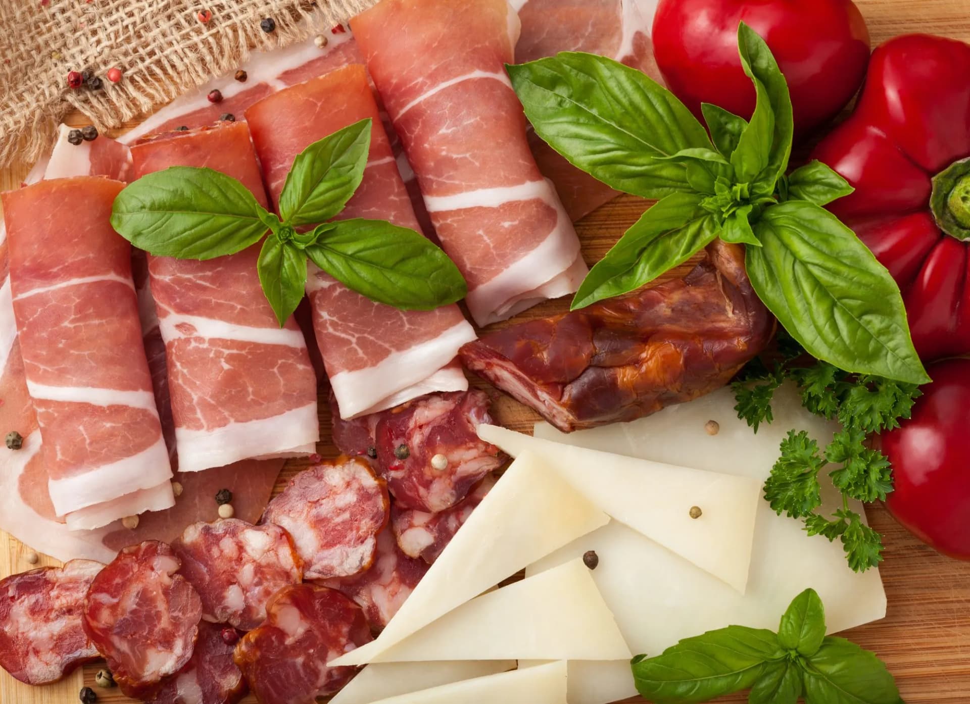 Cured meats, cheese wedges, red peppers, and basil garnish on a wooden board