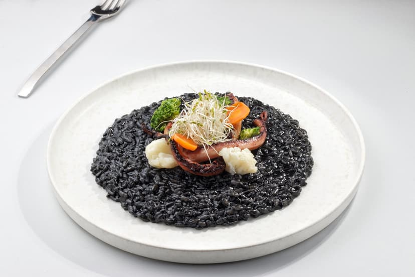 Black squid ink risotto with grilled octopus and vegetables on a plate