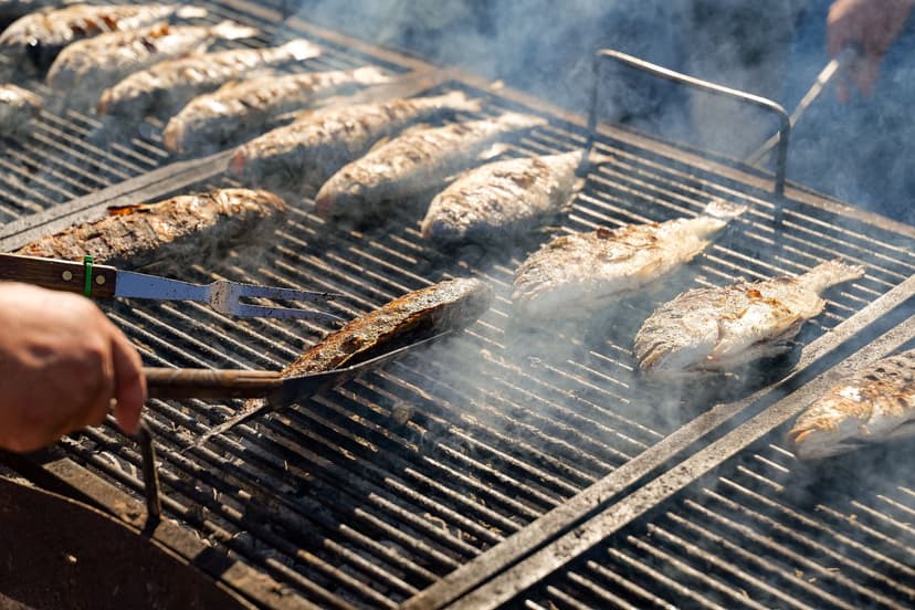Grilled fish cooking on a large outdoor grate with smoke