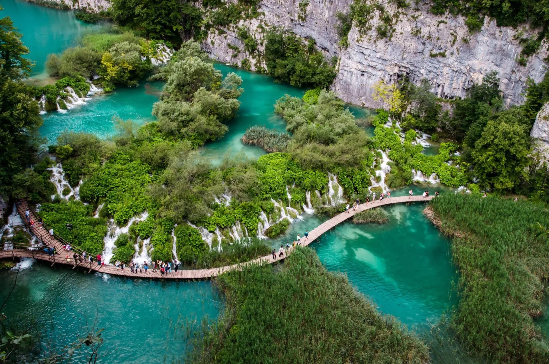 Wooden walkways winding over turquoise water with small waterfalls at Plitvice Lakes National Park.