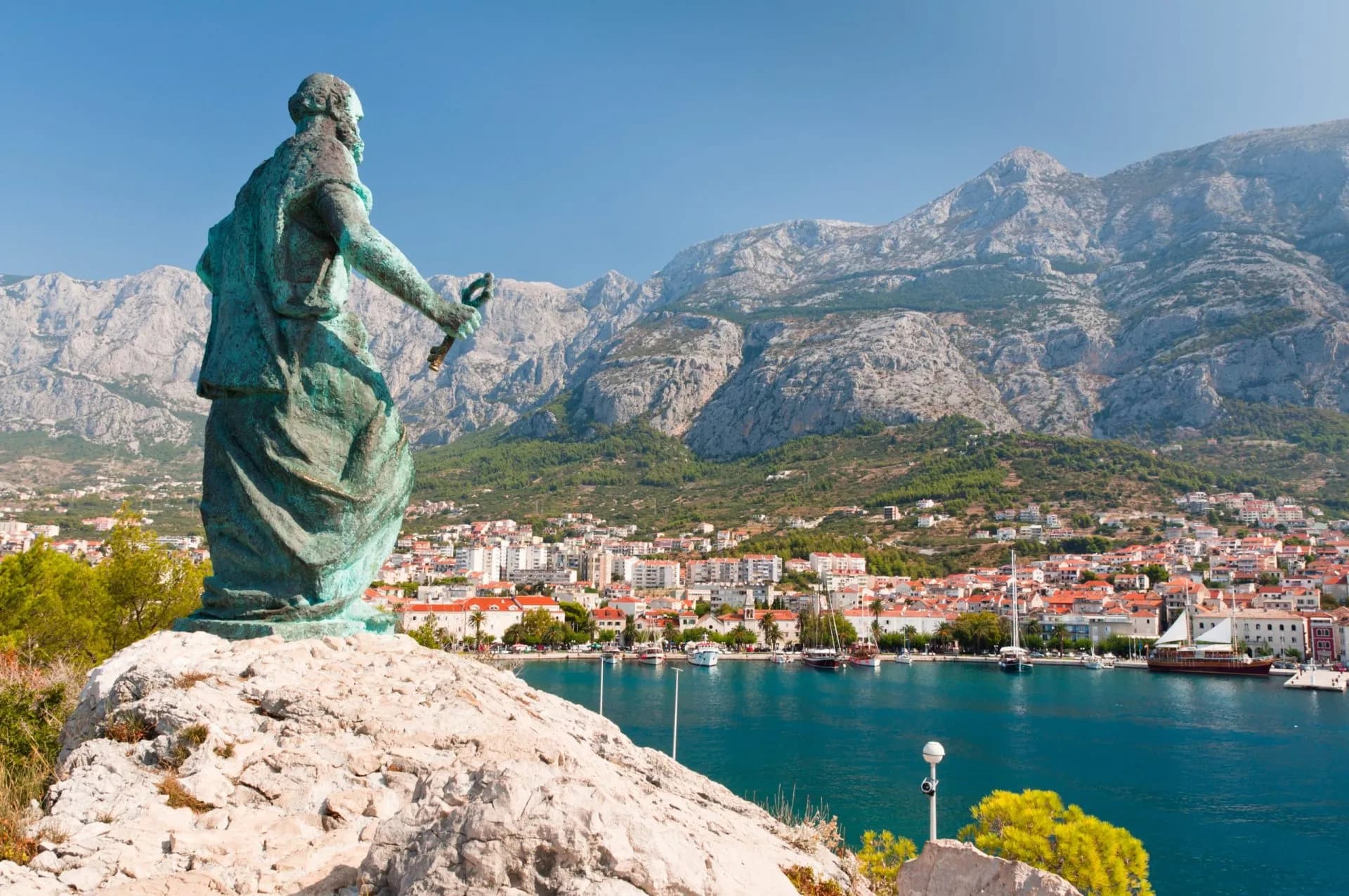 Bronze statue overlooking Makarska, Croatia, with harbor and Biokovo mountains.