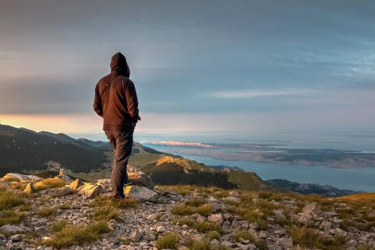 El alpinista de pie en la cima del Alancic mountin en la cordillera Velebit fotografiar con el teléfono, Croacia